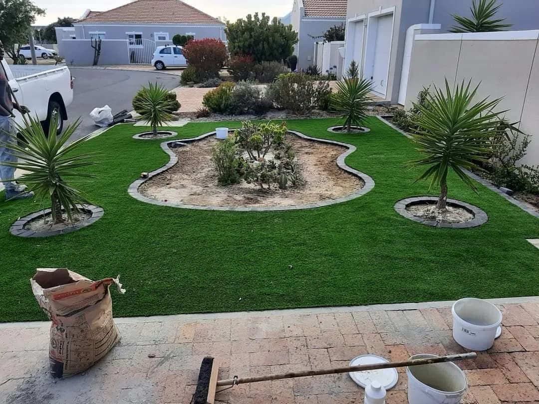 Front garden with artificial lawn surrounding a curved planted feature bed